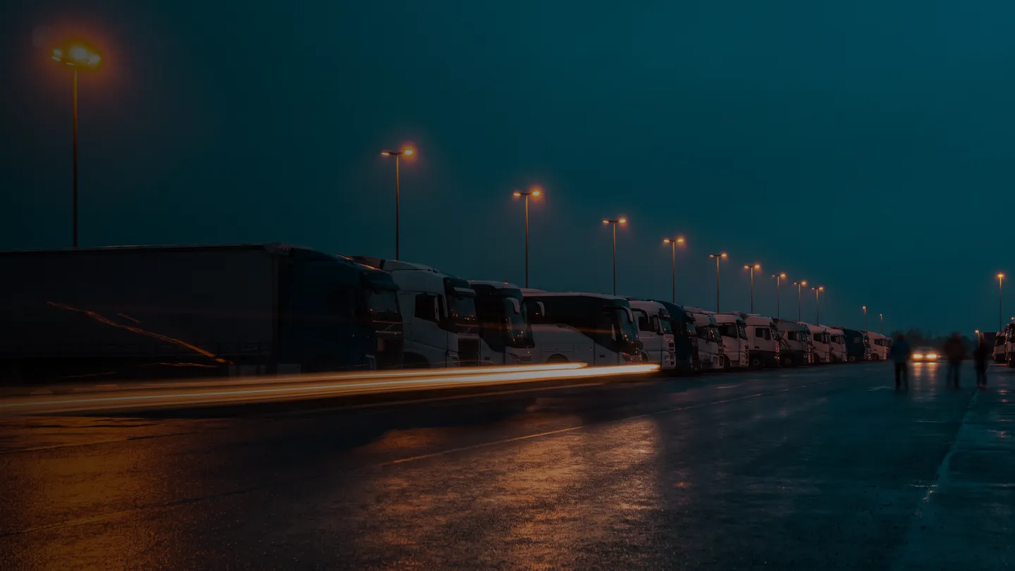 Alacakaranlıkta ışıklandırılmış tır ve otobüs filosu sıralanmış karayolu taşımacılığı merkezi